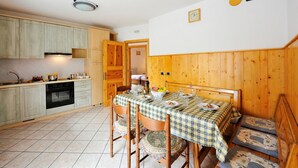 Een keuken met houten kastjes, een eettafel met een geruit tafelkleed en een bank met gestreepte kussens.
