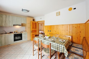 A kitchen with wooden cabinets, a dining table with a checkered tablecloth, and a bench with patterned cushions. - Camoscio Ski in - Ski out 200m, Livigno, Italy (Livigno)