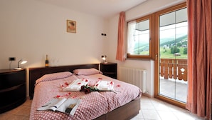 Een slaapkamer met een bed, een nachtkastje, een lamp, een raam met uitzicht en een radiator.