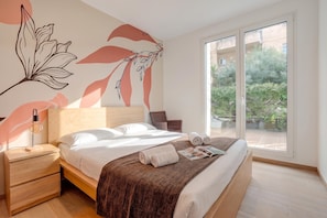 A modern bedroom with a large bed, a nightstand, a wall-mounted lamp, and a view of greenery through a sliding glass door. - Boutique Apartment Rebecca with private Garden close to the centre., Lugano, Switzerland (Lugano)