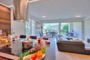 A modern kitchen with an induction cooktop, a dining area with a sofa, and a view of the outdoors.