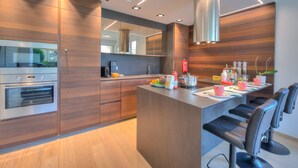 A modern kitchen with wooden cabinetry, a built-in oven, and a central island with bar stools. - Rebecca Garden with Terrace in Paradiso, Lugano, Switzerland (Lugano)