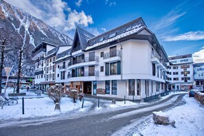 A multi-story hotel with balconies, a ski slope in the background, and a snow-covered street.