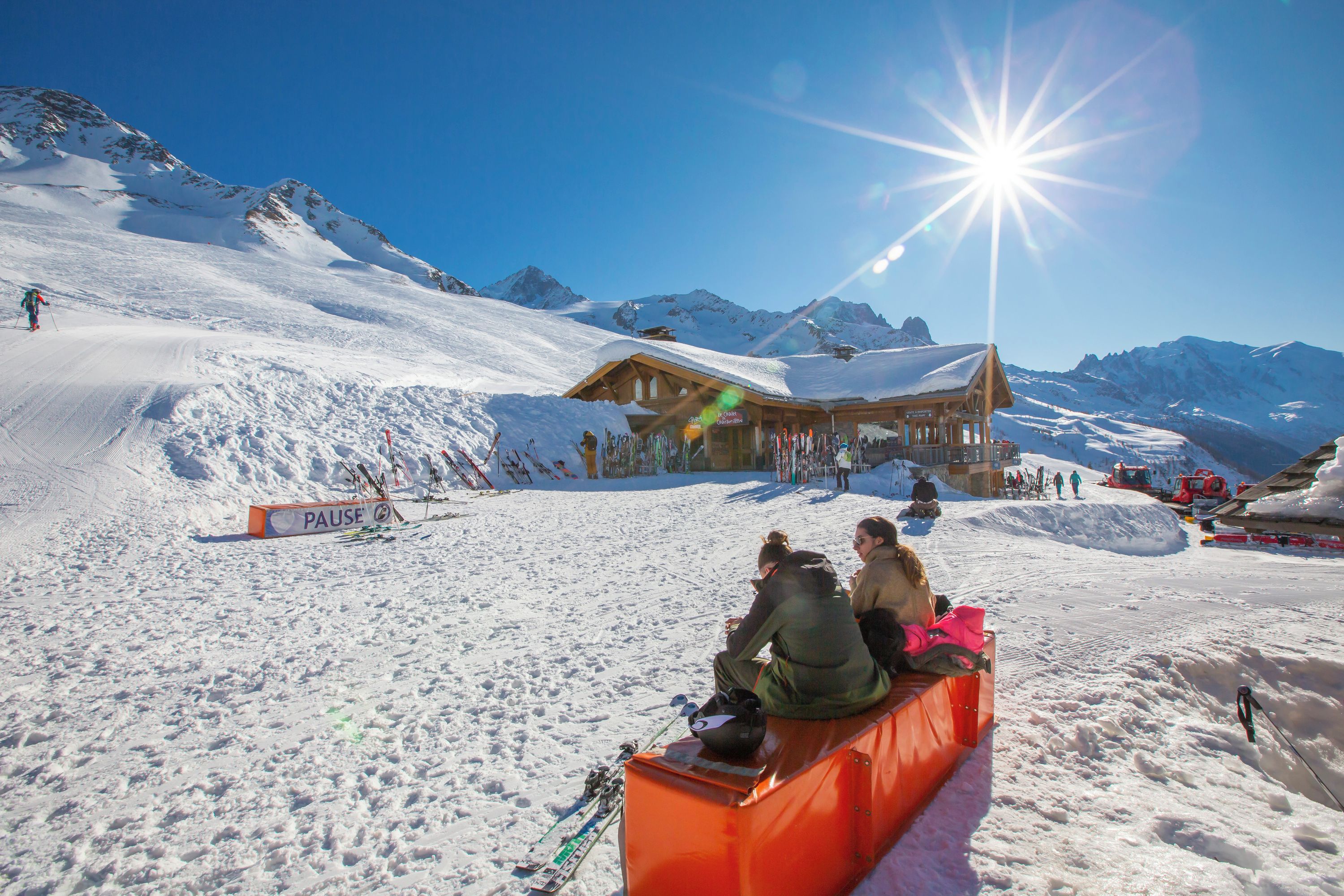 Une station de ski avec un chalet en bois, un panneau indiquant « Pause », et un ciel bleu dégagé.