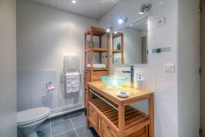 Uma casa de banho moderna com uma toucador de madeira, lavatório em taça de vidro, sanita e zona de duche.
