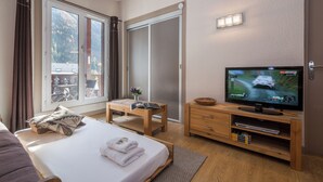 A hotel room with a bed, a television, a wooden dresser, a small table, and a sliding door to a balcony. - Cham Sud Forclaz504 - 1BR w/ Balcony sleeps 4, Chamonix, France (Chamonix)