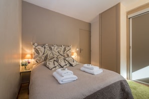 A neatly made bed with folded towels, a bedside lamp, and a floral-patterned headboard. - Cham Sud Forclaz504 - 1BR w/ Balcony sleeps 4, Chamonix, France (Chamonix)