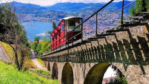 A cable car moving over a stone bridge with a city and mountains in the background. - Twin Home in Castagnola for 4, Lugano, Switzerland (Lugano)