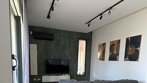 Un salon moderne avec un canapé gris, un téléviseur et des œuvres d’art abstraites accrochées au mur.