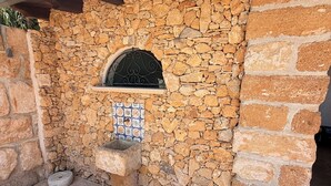 Un mur en pierre orné d’un motif de carreaux décoratifs, un banc en pierre et une fenêtre à cadre métallique.