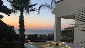 Un bain à remous dans un jardin, avec vue sur la mer au coucher du soleil.