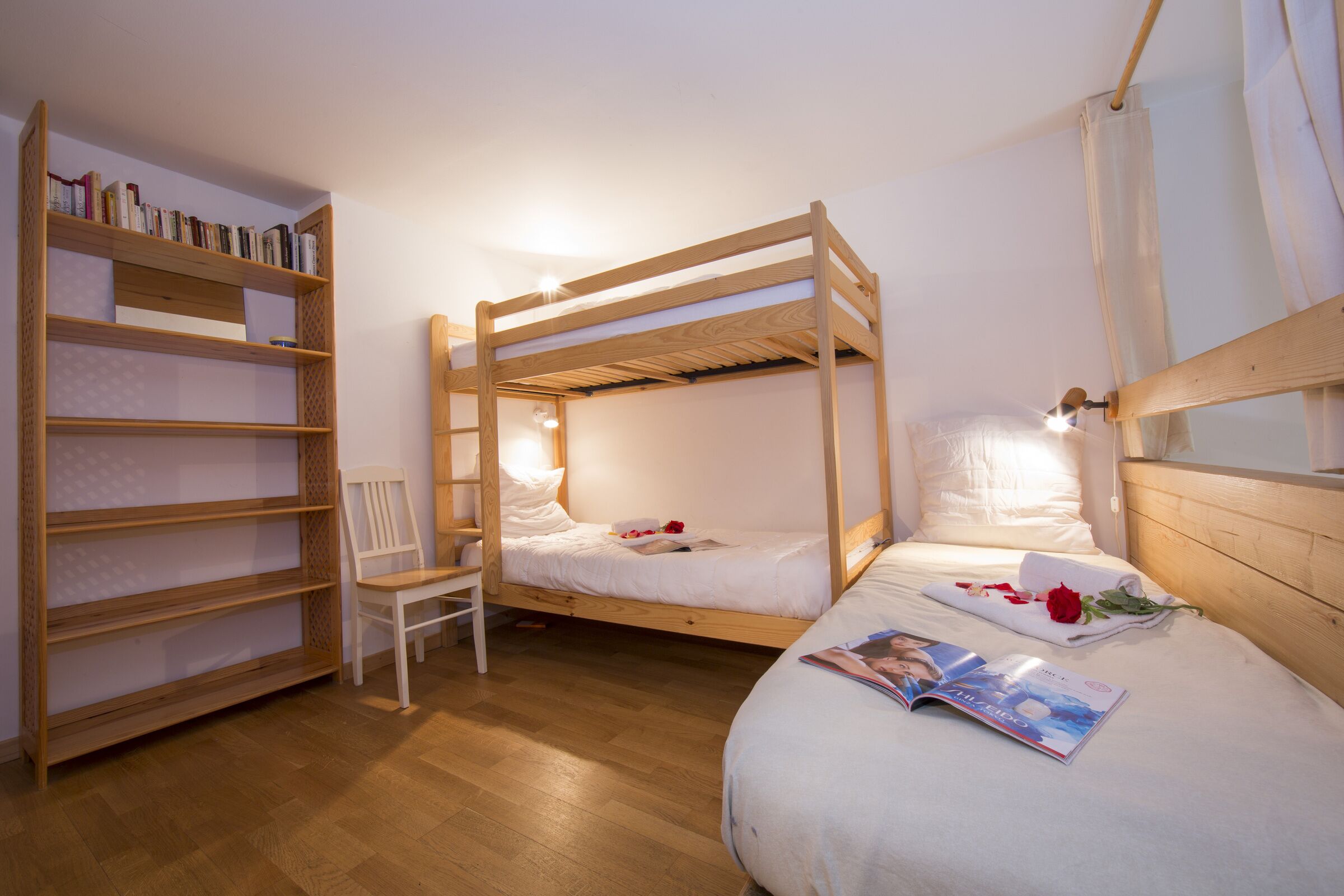 Ein Zimmer mit zwei Etagenbetten, einem Holzregal und einem Sessel.