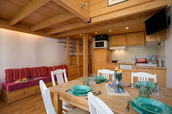 A wooden dining table set with green plates, glasses, and a vase with flowers. There is a wooden bench with colorful cushions in the background. - Grand Roc A220 150m from Slopes, View & Parking, Argentière (Chamonix), France (Argentière (Chamonix))