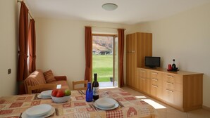 A dining area with a table set for two, a television, and a view of the outdoors.