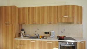 A kitchen with wooden cabinets, a sink, a kettle, and a stove.