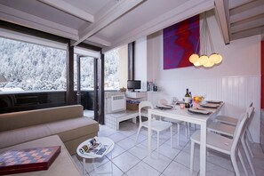 A modern living room with a sofa, a coffee table, and a dining area with a table set for two. - Grand Roc C303 280m from Slopes, View, Parking & WiFi, Argentière (Chamonix), France (Argentière (Chamonix))