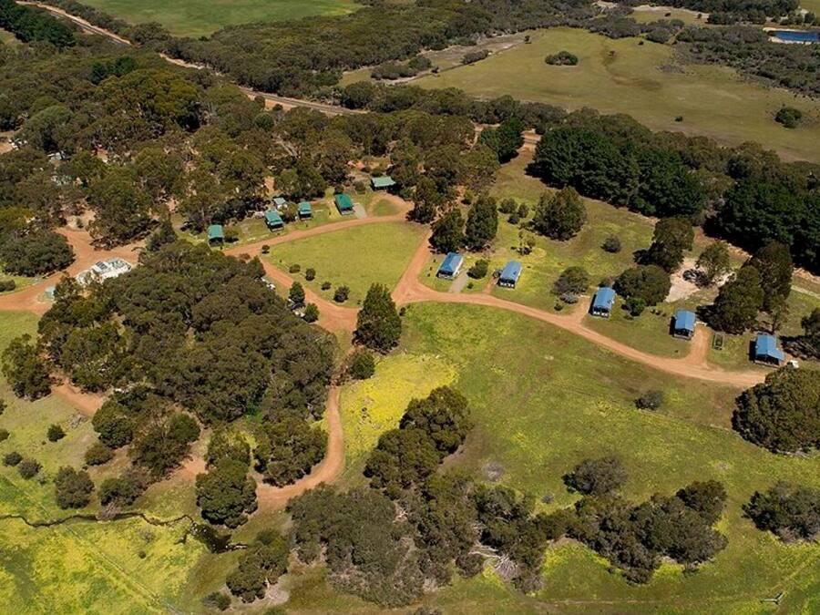An aerial view of a rural property with multiple buildings, surrounded by dense vegetation and open fields.