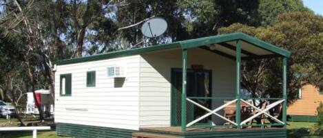 A small, single-story cabin with a porch, a satellite dish, and a small window.
