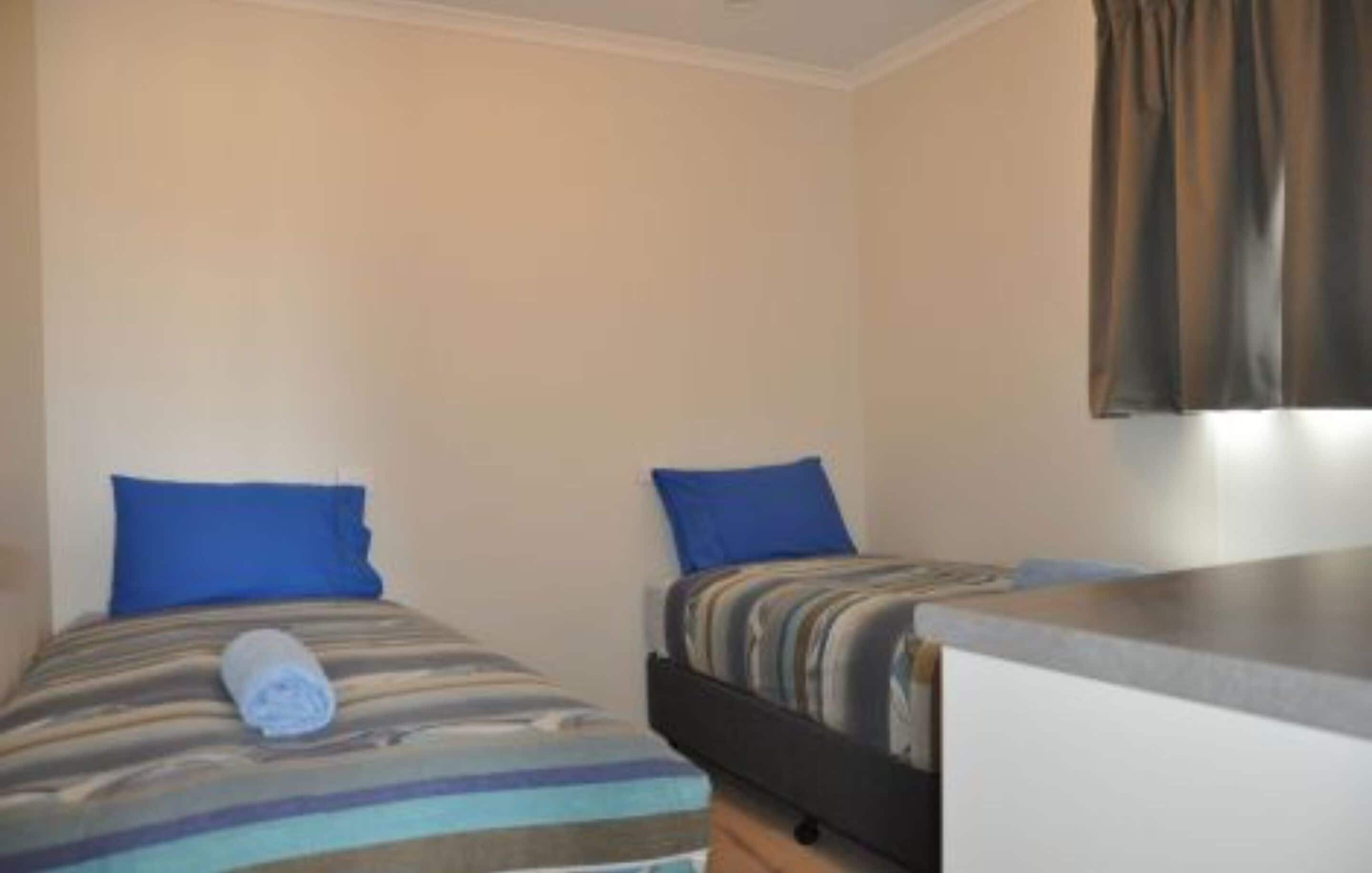 Un alojamiento pequeño de una sola habitación con dos camas, cada una con almohada azul y manta a rayas.