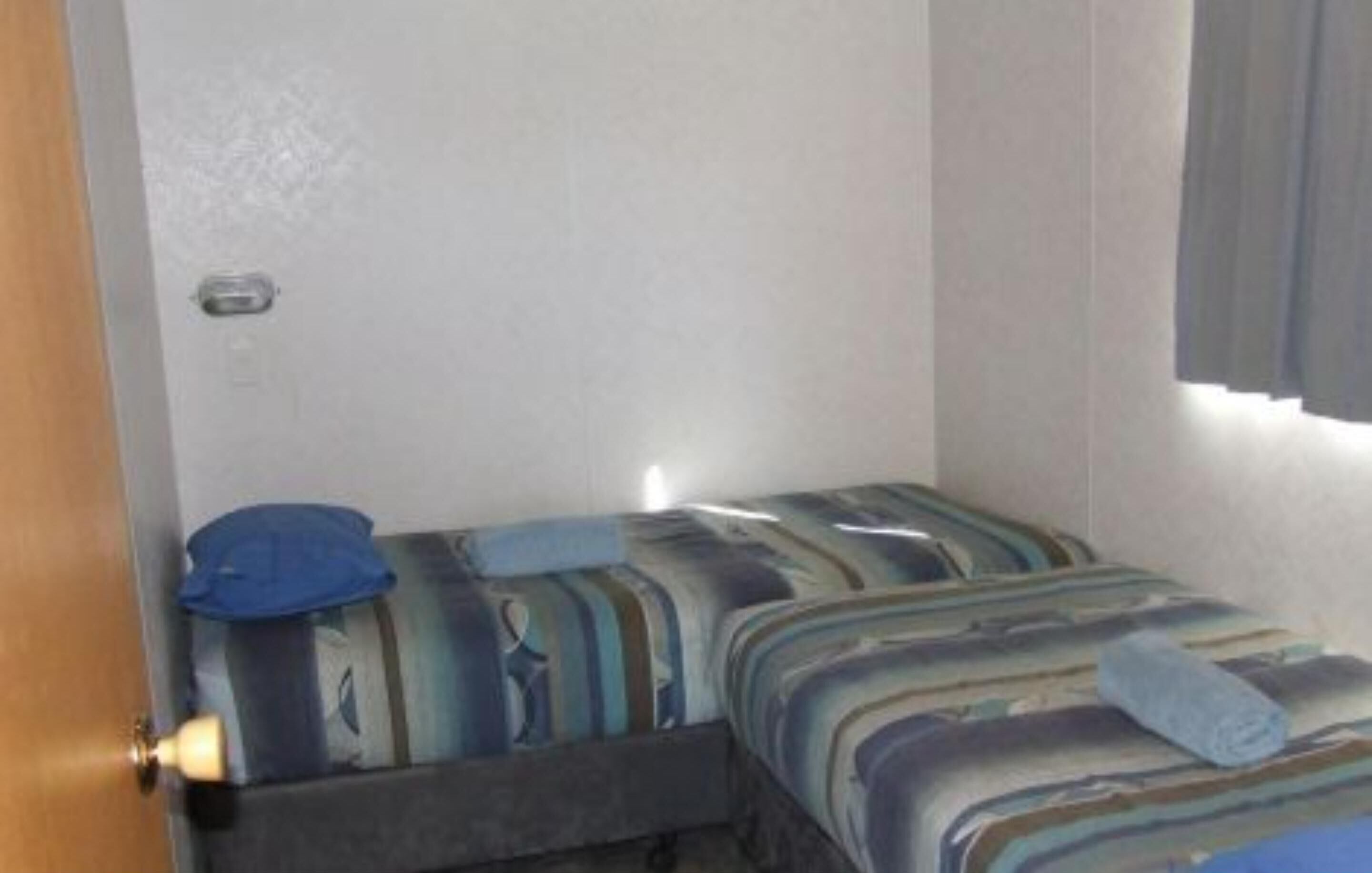 A small, single-bed room with striped bedding and a blue pillow.