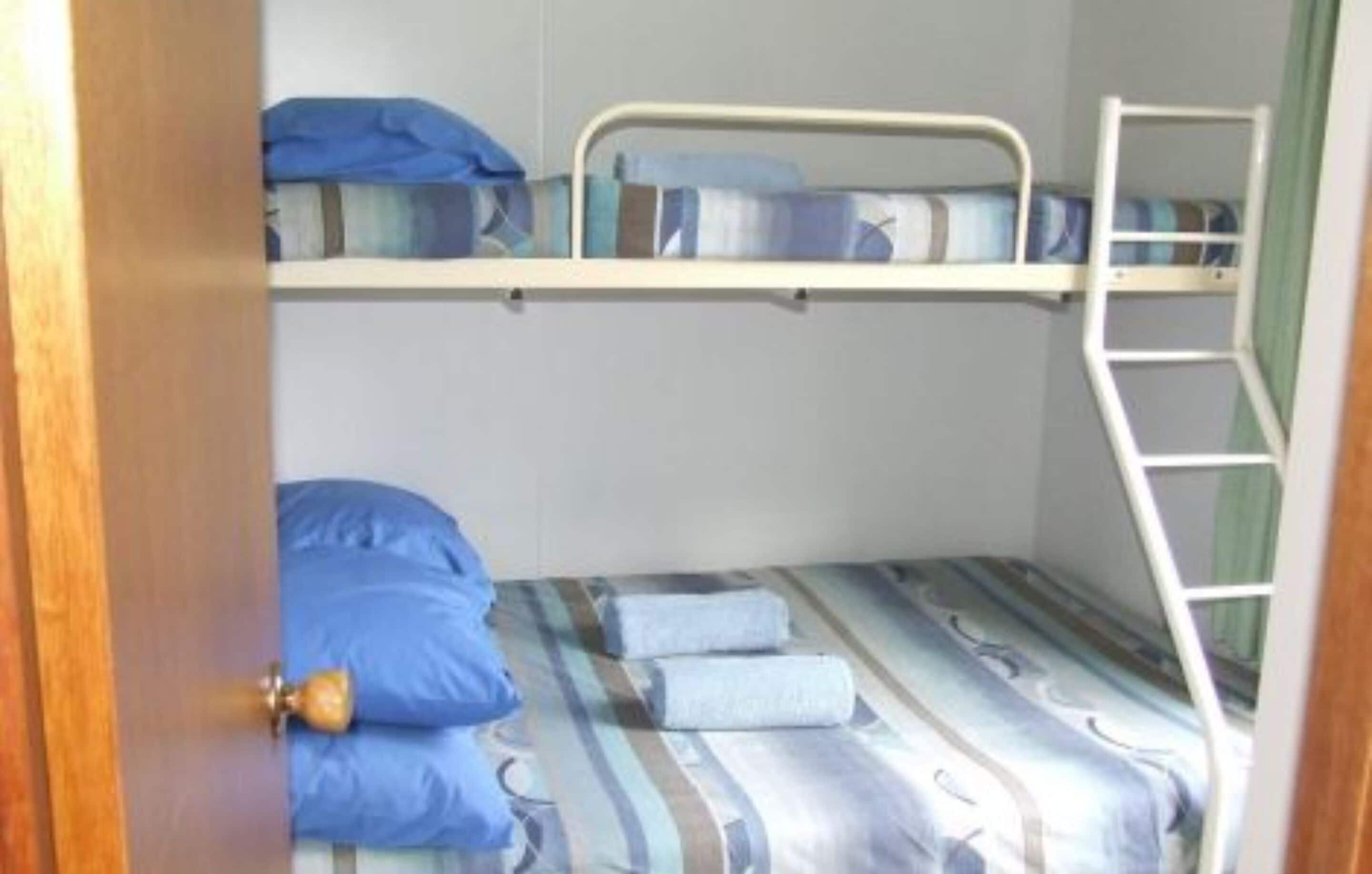 Een slaapkamer met een stapelbed, een ladder, een deur en een bed met een decoratief sprei.