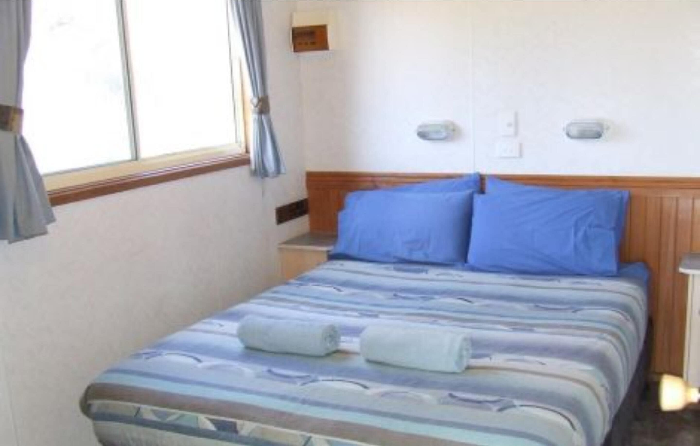 A single bed with a striped bedspread and two pillows, a bedside table, and a window with curtains.