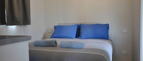 A bedroom with a bed, two pillows, a blanket, and a towel.