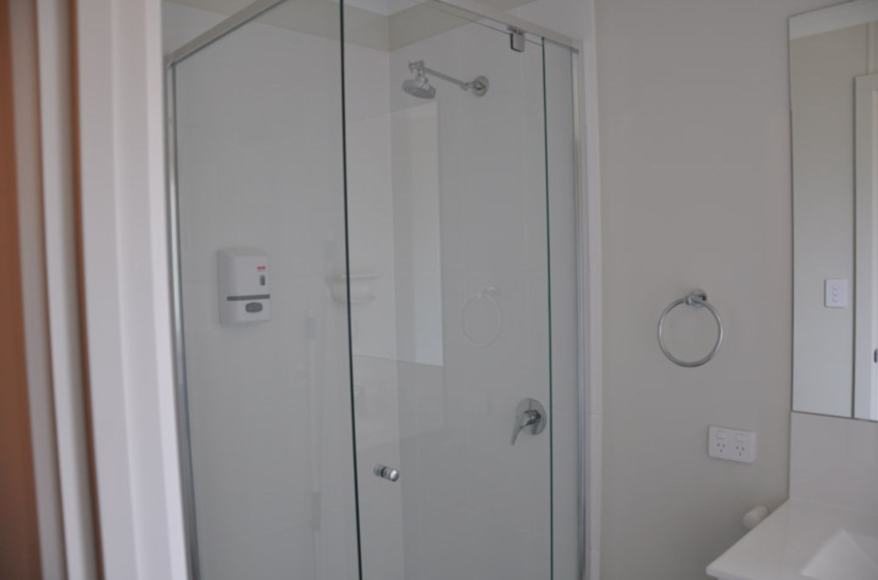 Een douche met glazen wanden, een handdouche, een handdoekhouder en een zichtbare stopcontact op de muur.