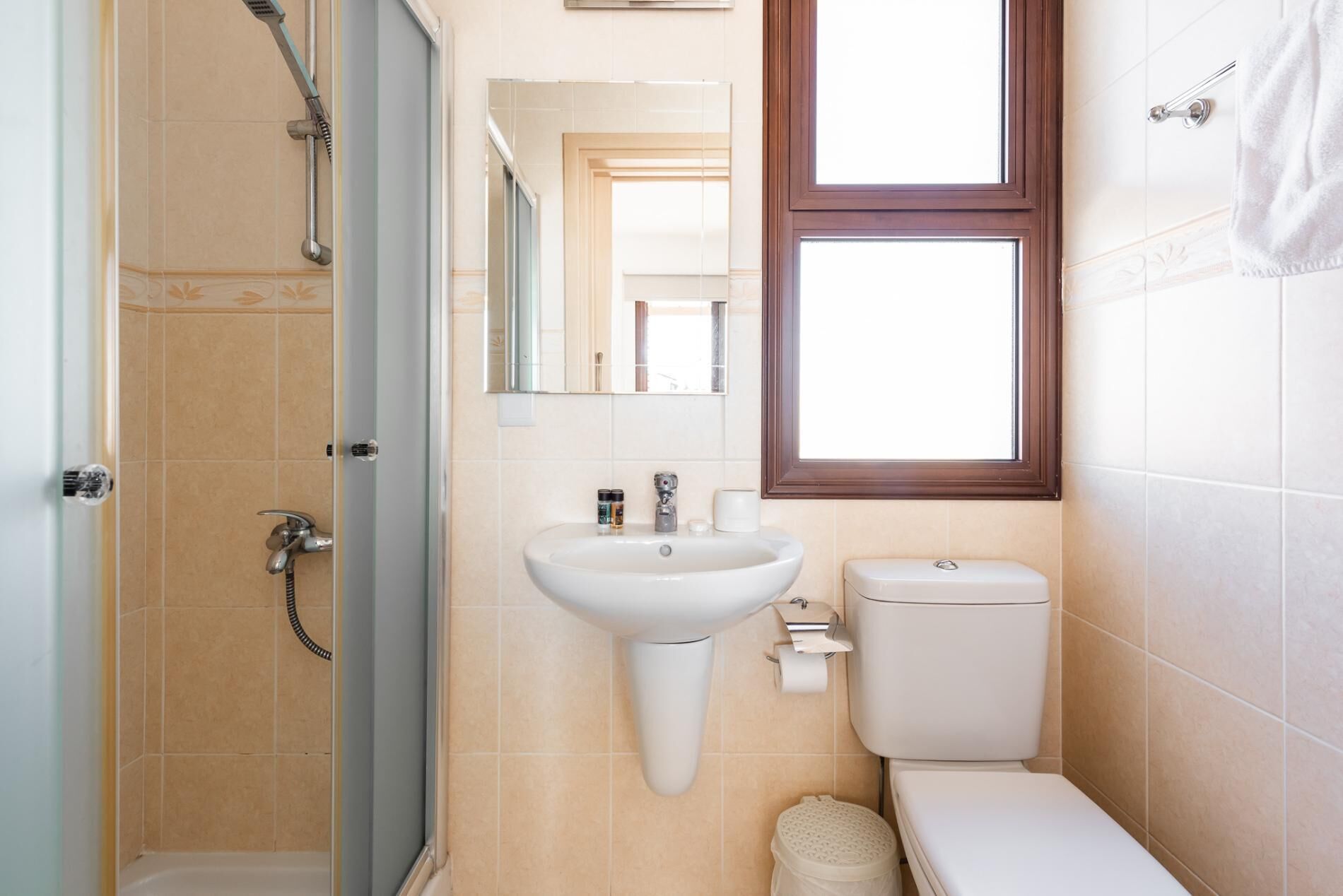 A bathroom with a shower, sink, toilet, and a window.
