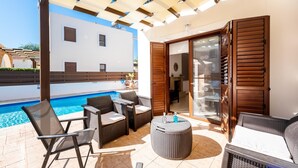 Ein überdachter Außenbereich mit Pool, Korbmöbeln und einer Glasschiebetür, die zu einem Raum führt.