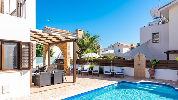 Ein Schwimmbecken mit Liegestühlen und Sonnenschirmen, einer Pergola sowie einem Grillplatz.