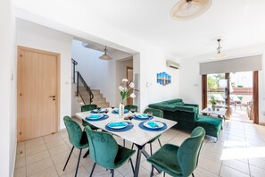 A dining area with a table set for four, green upholstered chairs, and a staircase leading to an upper level.