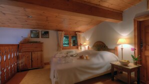 Une chambre avec un plafond en bois, un lit recouvert de draps blancs, une table de chevet avec une lampe et une fenêtre avec des rideaux.