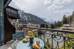 A balcony with a table set for two, a potted plant, and a mountain view.
