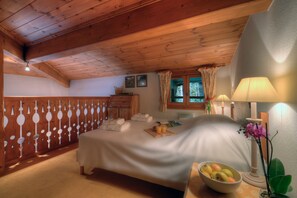 Une chambre avec un plafond en bois, un lit recouvert de draps blancs, une table de chevet avec une lampe et une fenêtre avec des rideaux.