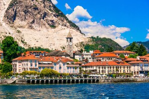 A coastal town with historic buildings, a prominent clock tower, and a rocky mountain backdrop. - Sunset in Baveno: 1 Bed with Balcony, Baveno, Italy (Baveno)