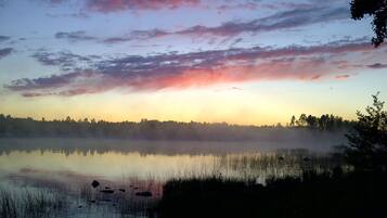 A calm lake at sunrise with a misty foreground and a forest in the background.