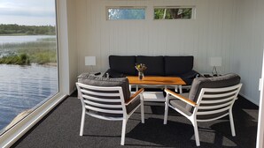 A room with a black sofa, two white chairs, a small table with a vase, and a view of a lake.