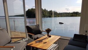 A deck with seating and a table, overlooking a calm lake with trees in the background.
