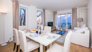 Un salon moderne avec un coin repas, des meubles blancs et de grandes fenêtres offrant une vue sur les montagnes.