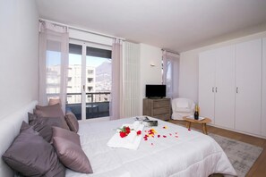A hotel room with a bed, a TV, a chair, a wardrobe, and a balcony with curtains.