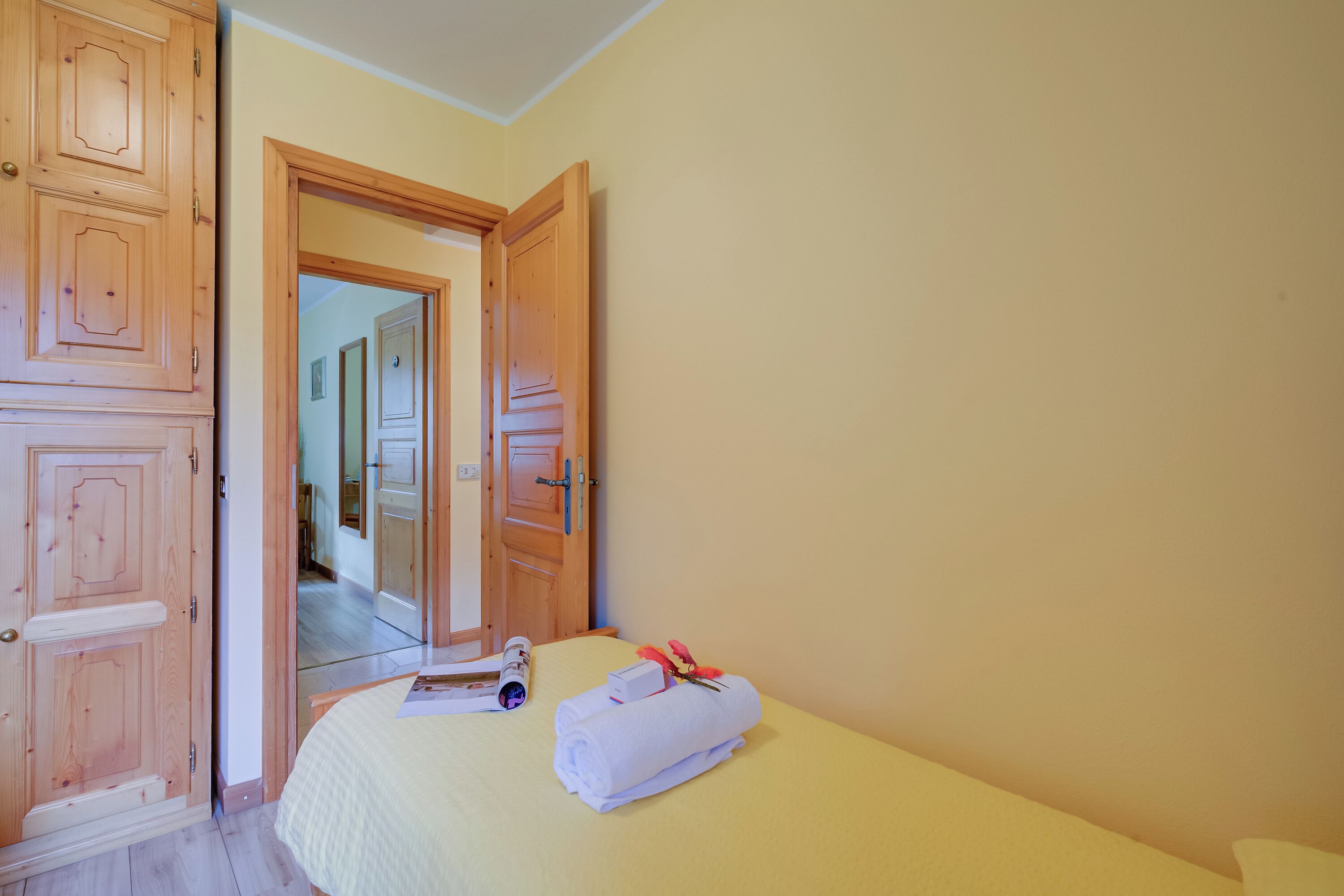 A hotel room with a bed, a wooden wardrobe, and a door leading to another room.
