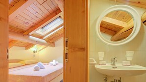 A wooden ceiling with skylights, a bed with a pink mattress, and a bathroom with a round mirror and sink.
