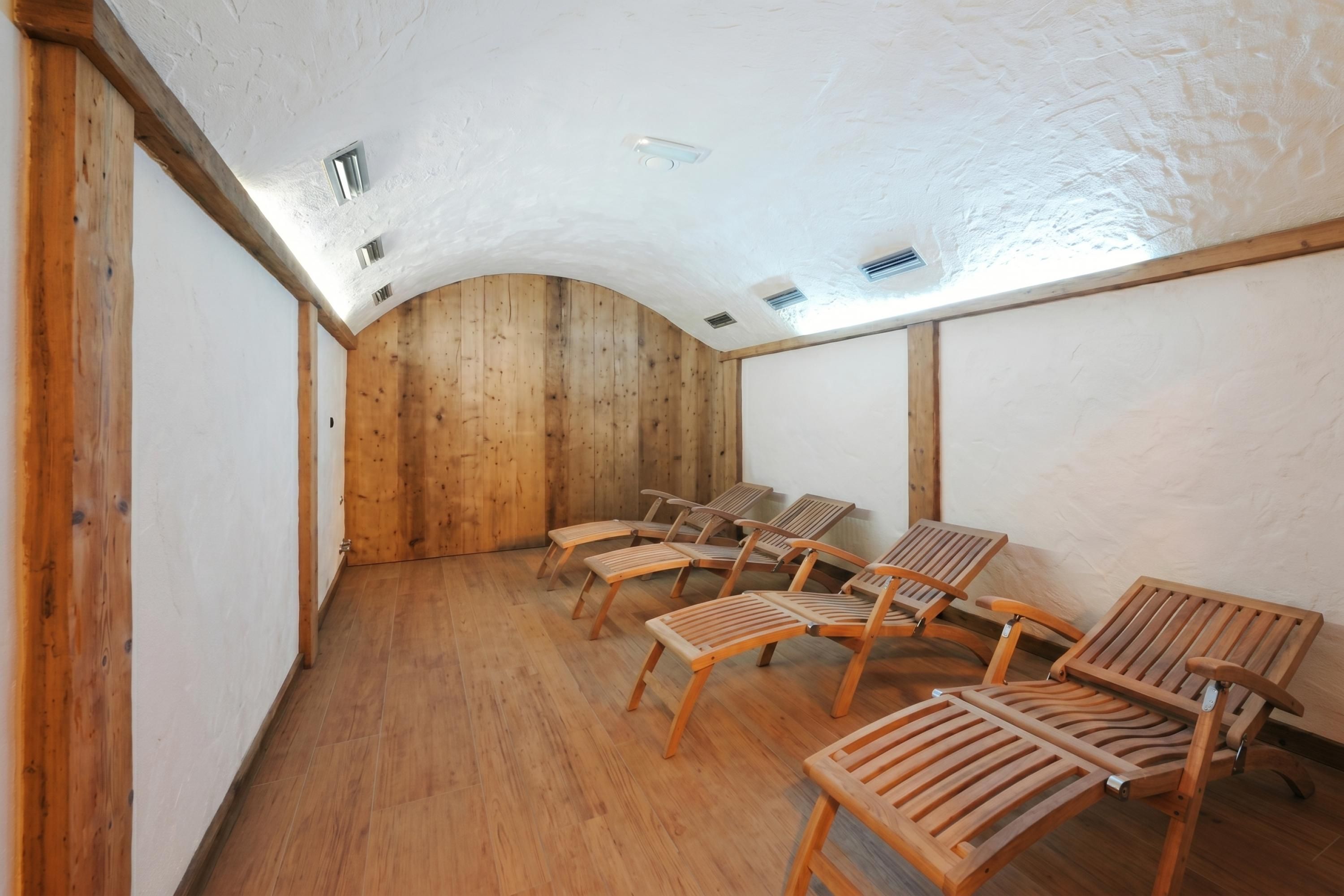 Una stanza con pareti e soffitto in legno, un tetto spiovente e diverse sedie in legno disposte per sedersi.