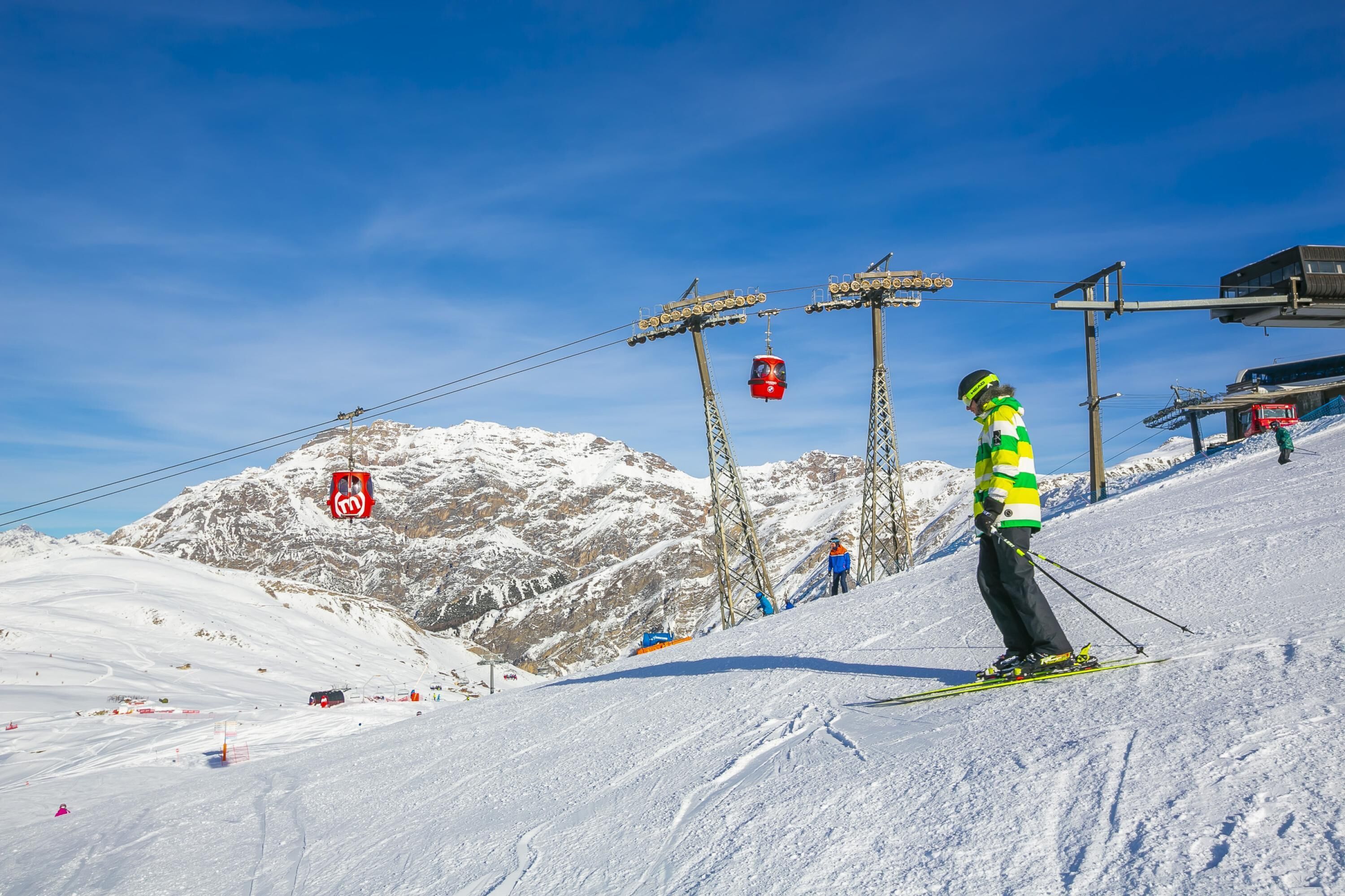 A ski slope with a person skiing, ski lift towers, and a mountain in the background.