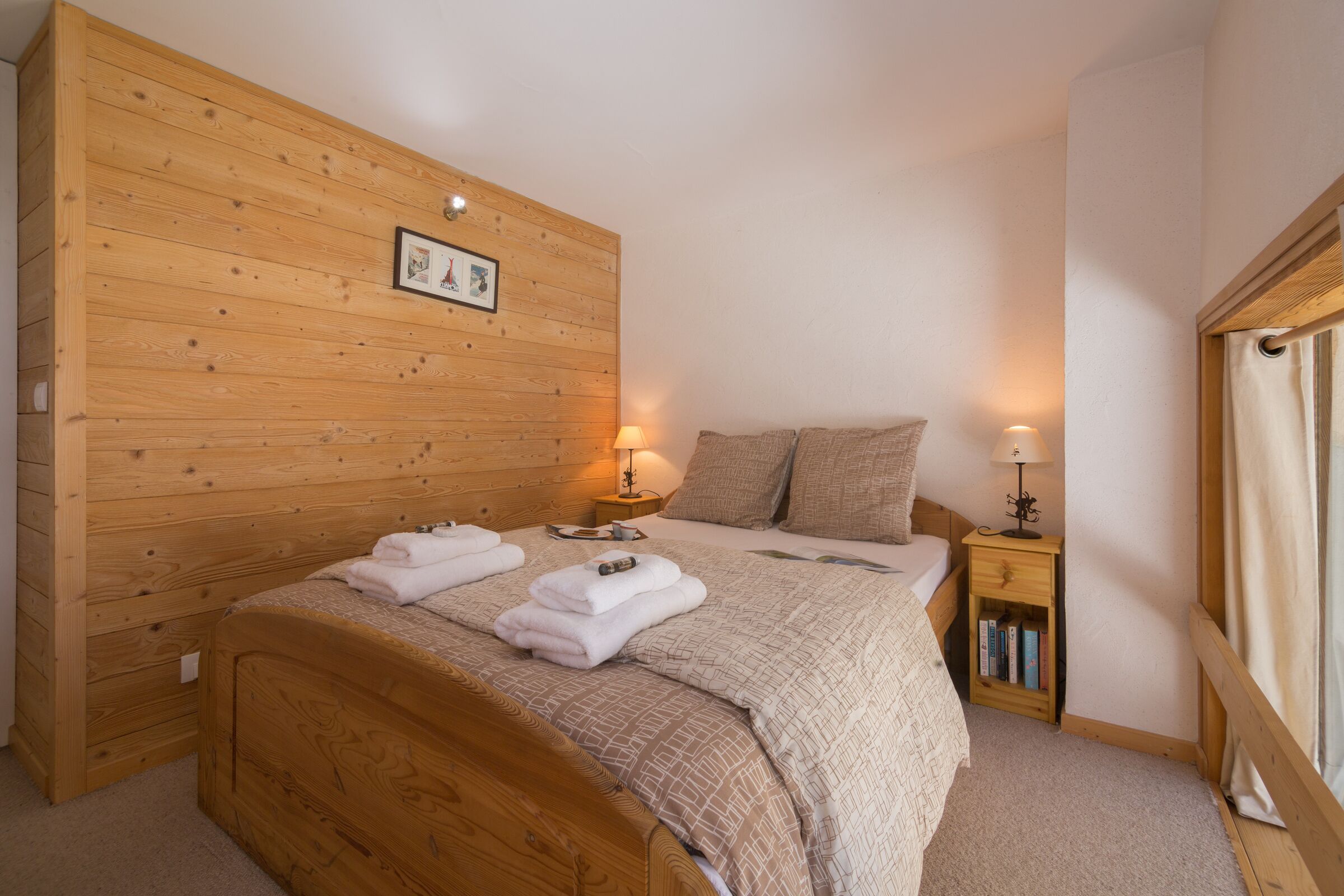 Une chambre à coucher aux murs lambrissés, avec un lit, deux tables de chevet et une petite table de nuit.