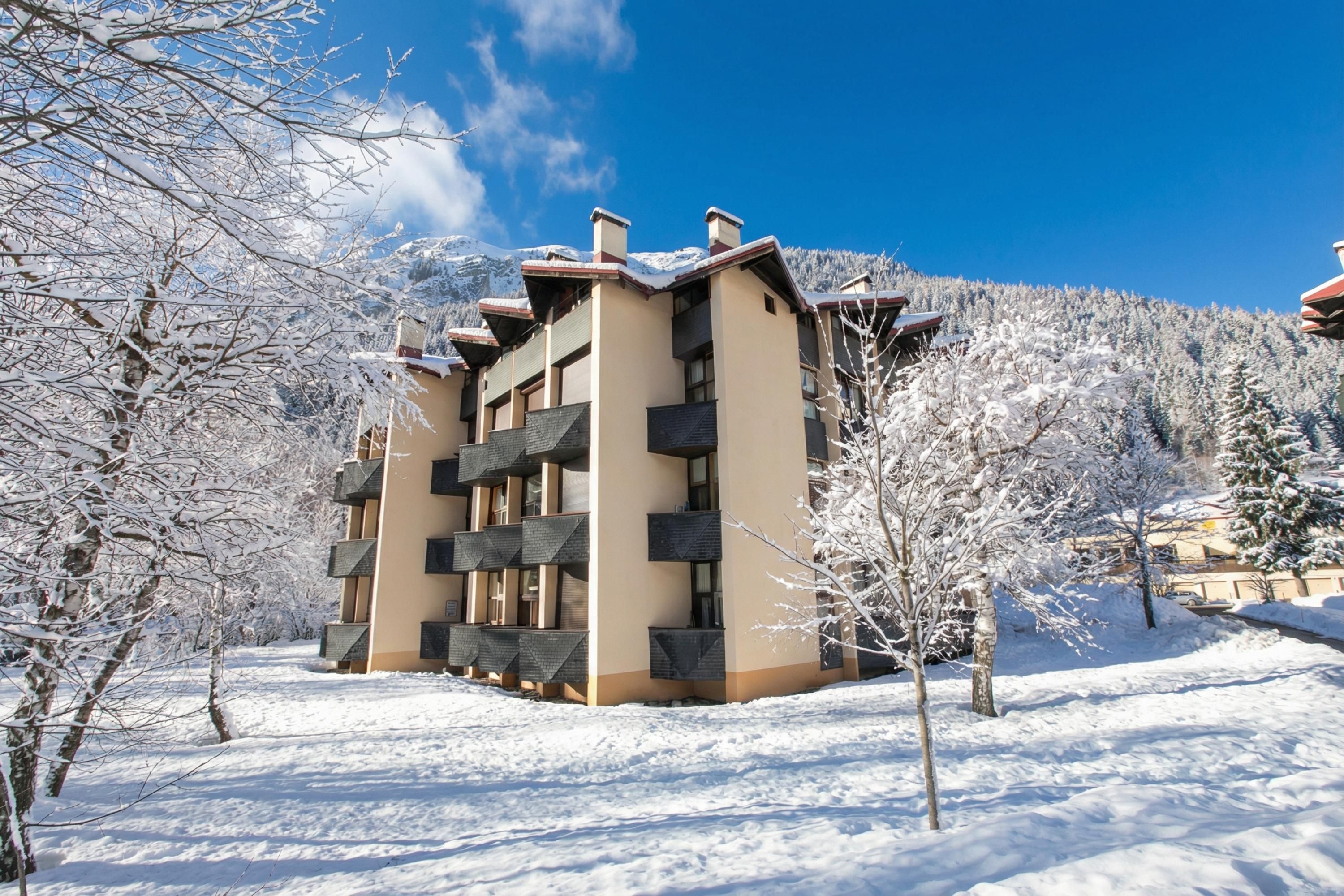 A multi-story building with balconies, surrounded by snow-covered trees and a clear sky.