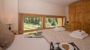 A bedroom with a large window, a bed, a bedside table with a lamp, a wooden wardrobe, and a view of greenery outside. - Grand Roc B220 260m from Slopes, View, Parking & WiFi, Argentière (Chamonix), France (Argentière (Chamonix))