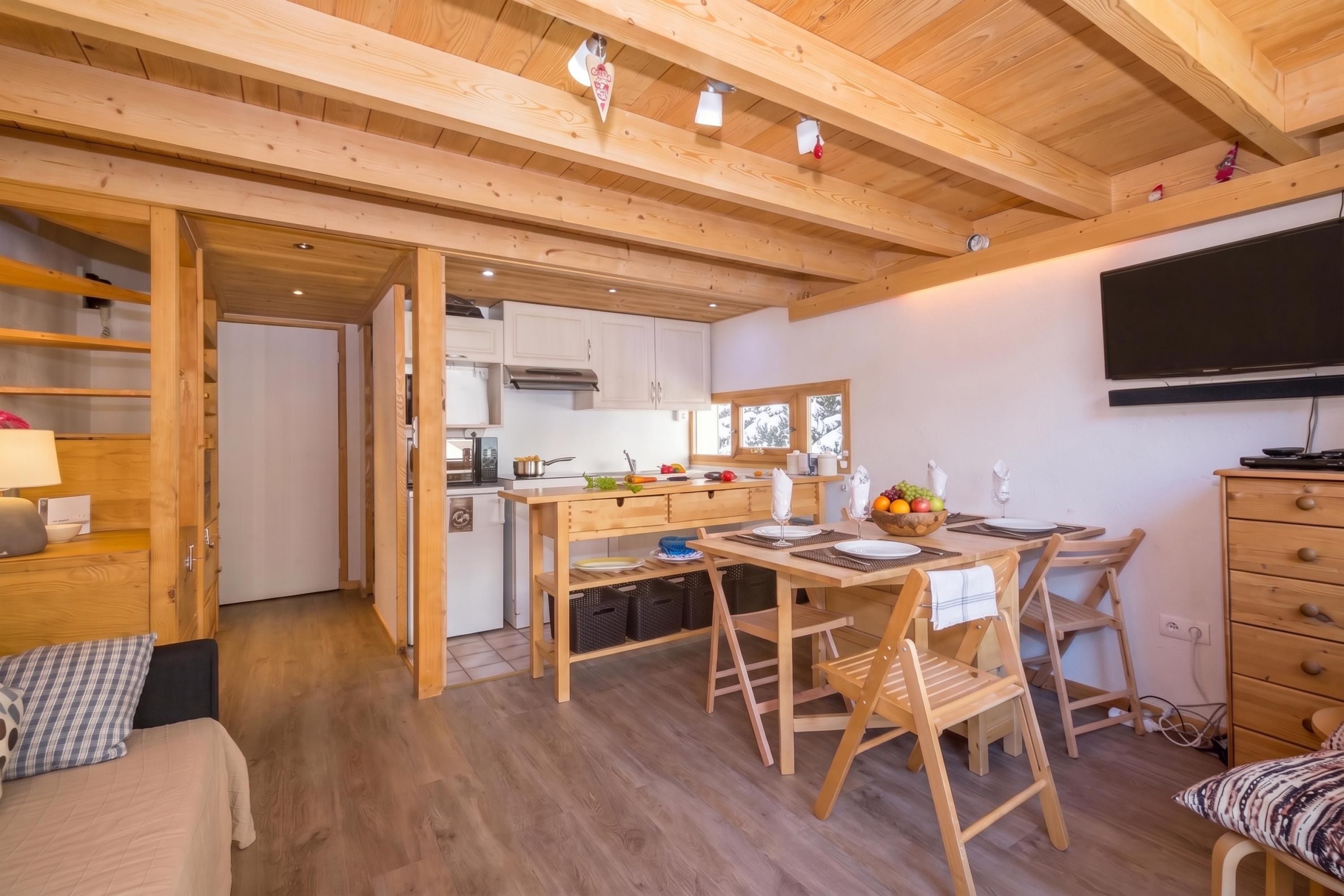 L’intérieur chaleureux d’un chalet comprend un coin repas, une cuisine et un téléviseur fixé au mur.