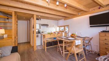 L’intérieur chaleureux d’un chalet comprend un coin repas, une cuisine et un téléviseur fixé au mur.